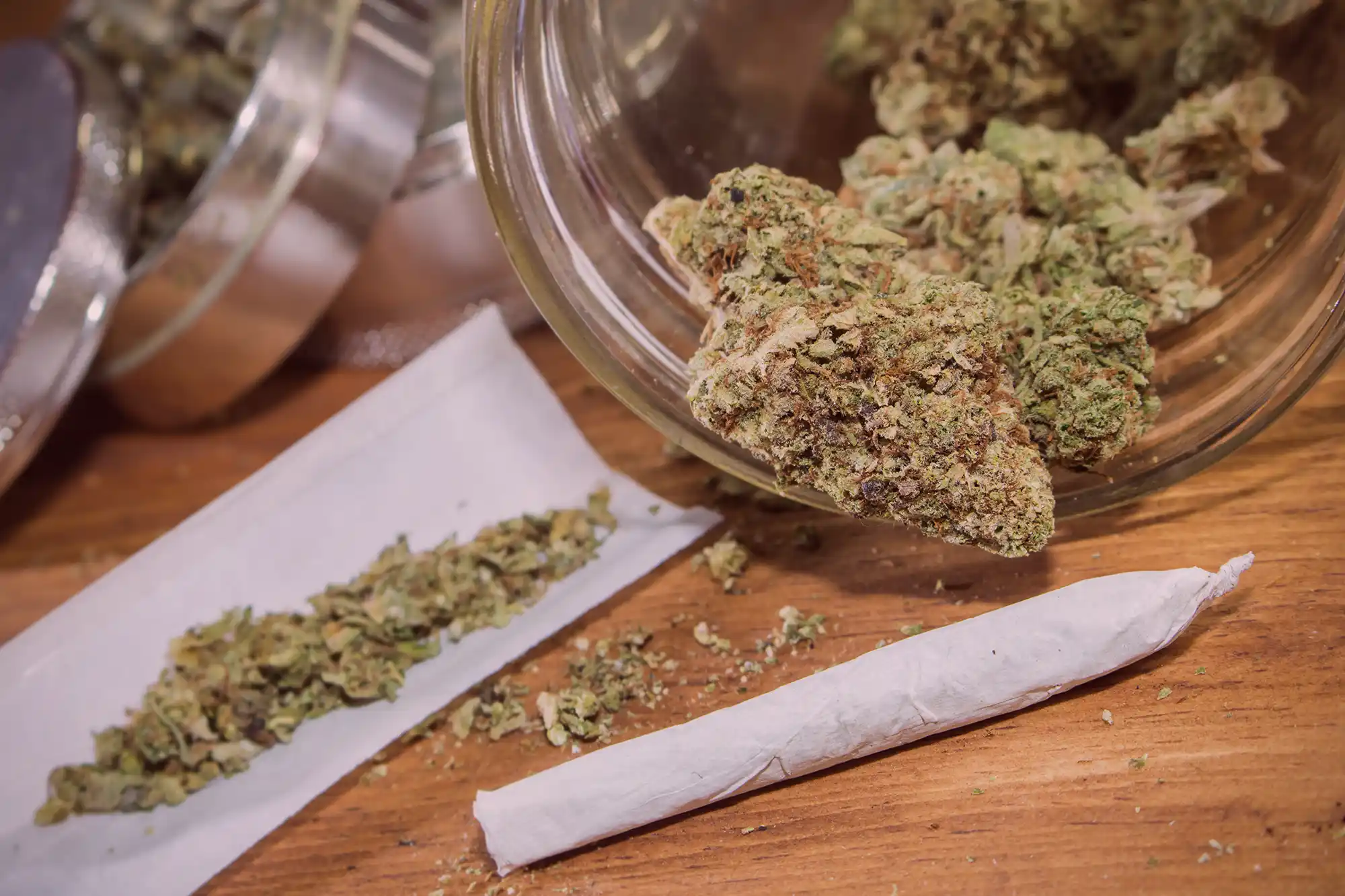 Cannabisblüten in einem Vorratsglas und ein fertig gedrehter Joint auf einer Holzunterlage. Visualisierung von Cannabisbesitz und der Gefahr der Überschreitung gesetzlicher Grenzwerte nach KCanG.