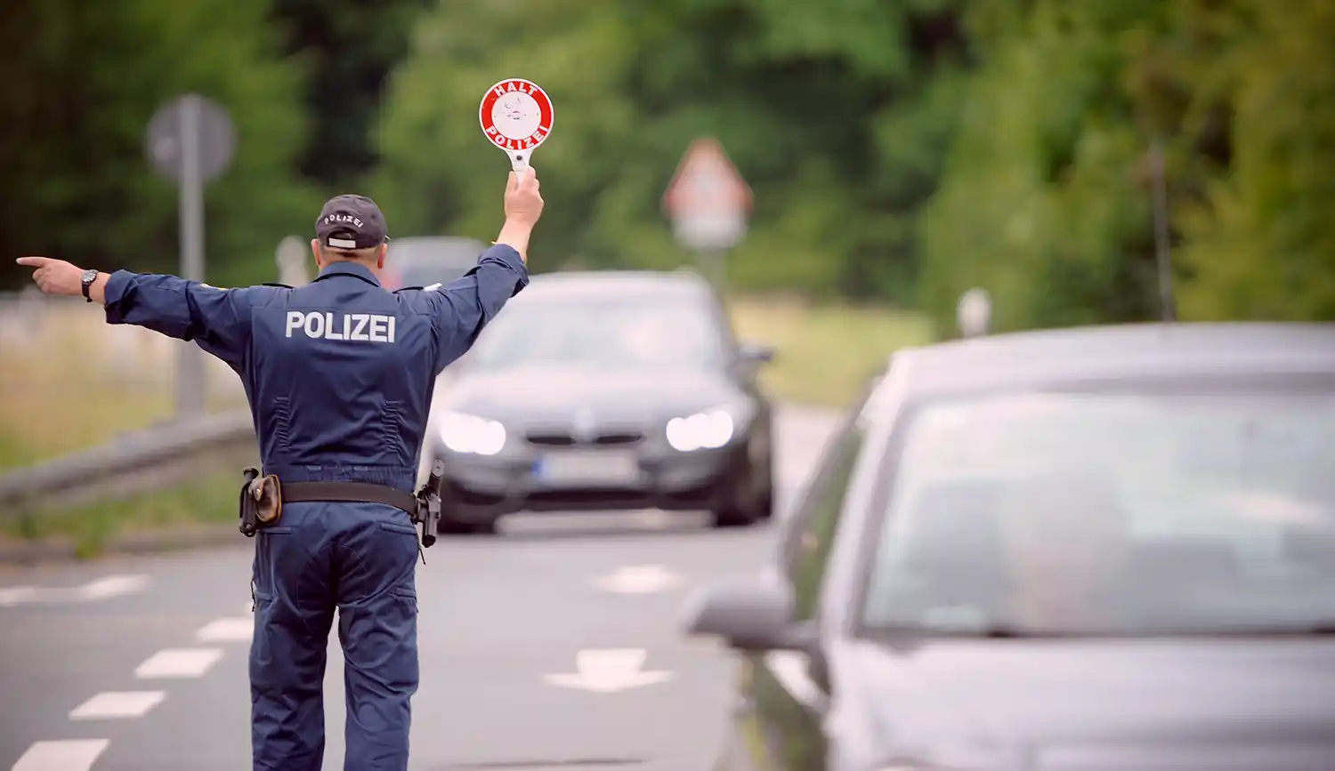 Ein Polizeibeamter hält mit einer Signalkelle ein Auto an. Symbolbild für eine Verkehrskontrolle auf Drogen am Steuer (Cannabis) und drohenden Führerscheinentzug.